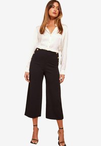 Vit skjorta med knappar, kombinerad med högmidjade svarta culottes med detaljer i guldknappar. Svarta sandaler med remmar fulländar looken.
