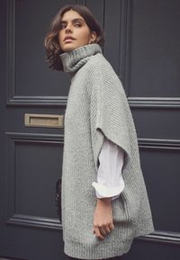 Maglione girocollo grigio chiaro a coste con vestibilità over size, dotato di maniche corte e un finish texturizzato. Una camicia bianca spunta da sotto.