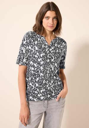 Haut à manches courtes avec un motif abstrait noir et blanc, présentant un design sans col et en tissu doux. Associé à un jean gris clair.