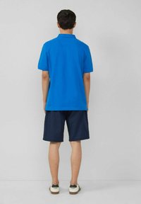 Blauses Poloshirt mit kurzen Ärmeln, kombiniert mit dunkelblauen Shorts. Das Hemd hat ein klassisches Kragen-Design, und der Look wird mit weißen Sneakers abgerundet.