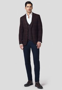 Kostium w brązową kratę na ciemnej kamizelce, biała koszula i granatowe spodnie. Brązowe buty dopełniają stylizację. Dopasowany krój i strukturalny design.