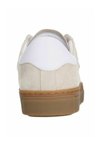 Beige suède sneaker met een witte leren hielkap en een bruine rubberen zool. De sneaker heeft een zachte textuur en een ronde vorm.