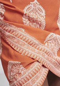 Tela naranja con intrincados patrones florales y de paisley en blanco, con una textura suave y un diseño fluido. Destaca por sus bordes detallados.