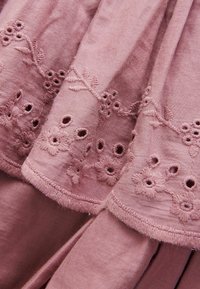 Rosa Stoff mit Stickerei, der florale Muster und Ausschnittdetails am Saum aufweist, weiche Textur mit einem leicht glänzenden Finish.