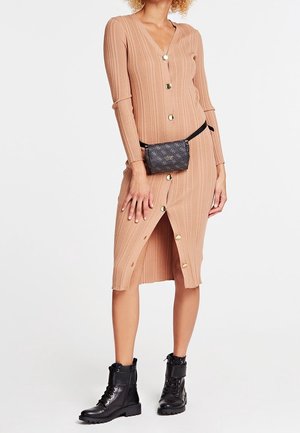 Femme portant une robe midi côtelée beige boutonnée, des bottes de combat en cuir noir et un sac ceinture noir à motif à la taille.