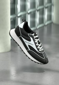 Scarpa da atletica bianca e nera con un design elegante, caratterizzata da una tomaia testurizzata, lacci bianchi e una suola in gomma per una buona trazione.