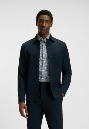 Navy button-up jacket over a black and white checkered shirt, featuring a chest pocket and smooth fabric for a tailored fit.