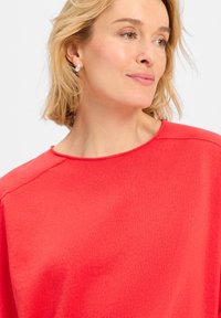 Rode trui met een brede, ronde halslijn, zachte textuur en verlaagde schoudernaden. Heeft een comfortabele pasvorm en minimale stikdetails.