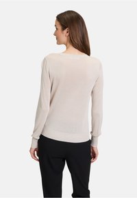 Pull long �à manches longues beige clair avec un col rond et des poignets côtelés, fabriqué à partir d'un tissu doux et léger, avec une texture légèrement transparente.