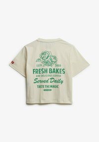 Lyscremet bomulds t-shirt med korte ærmer, prydet med grønne rosen grafik og tekst: "Friske bagværk, serveret dagligt, Smag magien. Superdry."