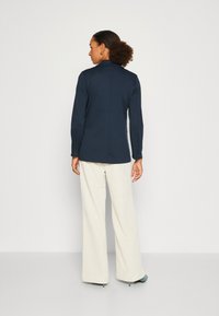 Chemise à manches longues navy avec col, texture lisse, coupe slim, associée à un pantalon large crème et des talons teal.