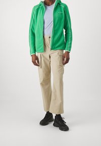 Green zip-up hoodie with textured fabric and white accents, paired with beige cargo pants featuring side pockets, and black athletic shoes.