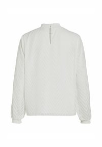 Blusa bianca con una texture a spina di pesce, maniche lunghe con polsini elasticizzati e chiusura a chiave sul retro. Tessuto morbido e leggero.
