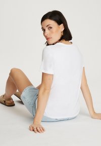 Biała, krótka koszulka z rękawem, z okrągłym dekoltem, w połączeniu z jasnoniebieskimi szortami dżinsowymi. Gładki materiał, prosty design, minimalistyczny styl.