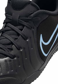Zapatilla deportiva negra con parte superior de cuero texturizado y malla, cordones negros y un logo de swoosh en azul claro. Diseño estructurado con suela de tracción.