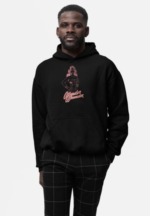 Czarna bluza z kapturem z różową grafiką i napisem Wonder Woman. Posiada kieszeń kangurkę oraz luźny krój, zestawiona z spodniami w kratkę.