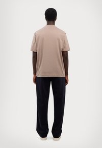 Beige bavlněné tričko s krátkým rukávem, volnějšího střihu a kulatým výstřihem, doplněné modrými širokými kalhotami a béžovými botami.