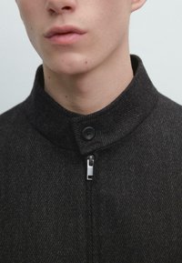 Czarna kurtka w jodełkę z wysokim kołnierzem, zapinana na zamek z przodu oraz guzikiem. Miękka w dotyku i dopasowana.