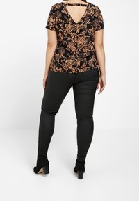 Haut noir à fleurs avec un design dos en trou de serrure, associé à un pantalon noir ajusté. Le matériau semble lisse ; l'ensemble a une coupe cintrée.
