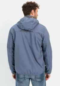 Lys blå, vandafvisende jakke med hætte, struktureret stof og sorte detaljer langs skuldrene og ryggen. Vandafvisende lynlås.