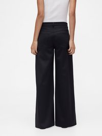 Pantalon noir à jambes larges avec une texture lisse, taille haute et poches arrière, offrant une coupe ample des hanches à l'ourlet.