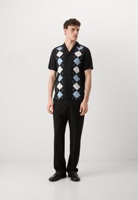Chemise noire à manches courtes avec un motif en losange bleu et blanc, dotée d'un col traditionnel et d'une fermeture à boutons, assortie à un pantalon noir.