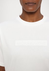 Λευκό βαμβακερό μπλουζάκι με ιονική ανάγλυφη λογότυπο "MICHAEL KORS" μπροστά, με κλασική στρογγυλή λαιμόκοψη και κοντά μανίκια.