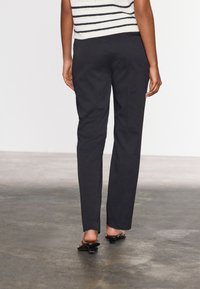 Svarta skräddarsydda byxor med rak passform, slät tyg och minimal sömnad. Bärs med en randig, kort topp och öppna skor.