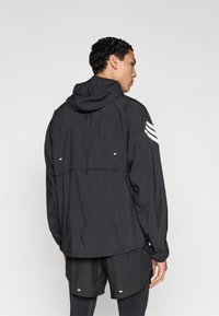 Zwarte lichte jas met capuchon, voorzien van witte strepen op de mouwen en reflecterende accenten, ontworpen voor sportkleding.