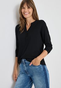 Svart långärmad tröja med henley-krage, tillverkad av mjukt tyg, i kombination med ljusblå jeans med smal passform och avsmalnande ben.