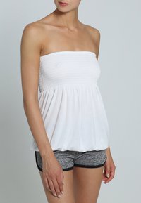 Weißes, trägerloses Oberteil mit einem gerafften Oberteil und fließendem Saum. Kombiniert mit grauen Sportshorts mit schwarzem Saum. Glatte Stoffstruktur.