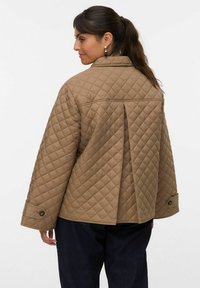 Veste beige matelassée avec des manches larges, motif de couture visible et détail de pli au dos. Accent de bouton sur les manches. Coupe décontractée et ample.