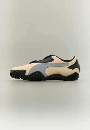 Scarpa da ginnastica beige e nera con suola in gomma nera testurizzata e striscia laterale grigia, mostrata di profilo su sfondo neutro.