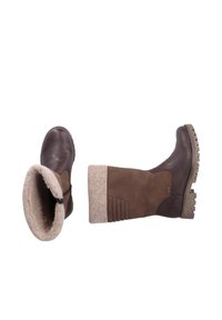 Brown leather boots with a soft, beige fabric cuff. Features a side zipper and textured rubber soles for grip. Vertical stitching detail visible.