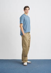 Polo T-shirt din bumbac de culoare albastru deschis, cu un buzunar pe piept, asociat cu pantaloni crem cu talie înaltă. Tenisi albi completează ținuta.