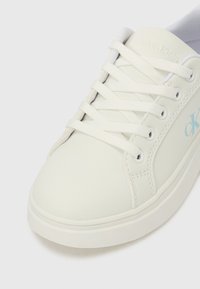 Sapatilha branca da Calvin Klein com atacadores brancos, biqueira arredondada e logótipo "cK" em azul claro na lateral.