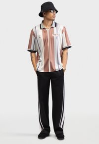 Striped polo shirt in brown, beige, and white with a black collar, paired with black track pants featuring white side stripes.