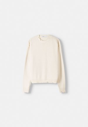 Langærmet sweater i cremefarve med ribstrikket rund halsudskæring, ærmer og kant, vist fladt på hvid baggrund.