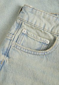 Svetlo modri jeans iz denima z žepom in srebrnimi gumbki na zapenjanje, vidno šivanje ter mehko teksturo. Podroben bližnji posnetek tkanine.
