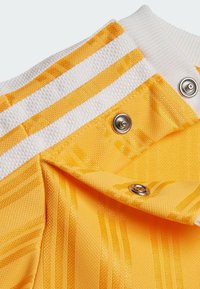 Il tessuto a strisce gialle presenta linee testurizzate, colletto a costine bianche e bottoni metallici, mettendo in risalto il suo design morbido e tessuto.