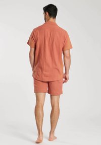 Ensemble chemise à manches courtes et short en tissu terracotta avec une finition texturée. La chemise présente un col et un dos avec un détail de empiècement.