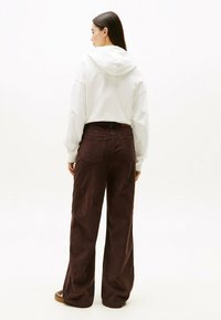Felpa bianca corta con cappuccio, abbinata a pantaloni larghi in corda marrone scuro con una finitura testurizzata e tasche posteriori.
