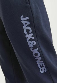 Joggers azul marino hechos de una tela suave con un gran logo en contraste "JACK&JONES" impreso verticalmente a lo largo del costado.