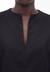 Κοντινό ενός ατόμου που φοράει μαύρο τοπ με V-σχήμα άνοιγμα στο λαιμό, εμφανίζοντας σκούρο δέρμα και την περιοχή του λαιμού.