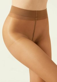 Collants transparents couleur beige avec une taille haute, texture lisse et un léger éclat, reposant sur la cuisse. Détail des coutures visible le long de la jambe.
