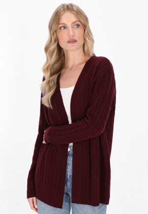 Bordeauxfarbener Strickcardigan mit Kabelmuster, offener Vorderseite und langen Ärmeln. Weicher Stoff, gerippte Bündchen und Saum. Kombiniert mit einem weißen Oberteil und Jeans.