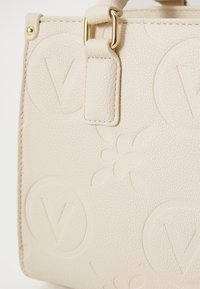 Beige strukturierte Handtasche mit dezenten geprägten Mustern und goldfarbenen Hardware-Details. Robuste Bauweise mit stabilen Griffen.