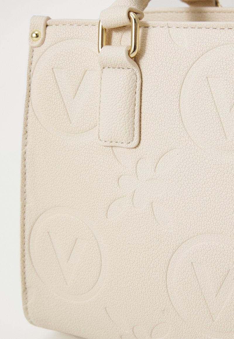Sac à main texturé beige avec des motifs en relief subtils et des détails en métal doré. Design structuré avec des poignées robustes.
