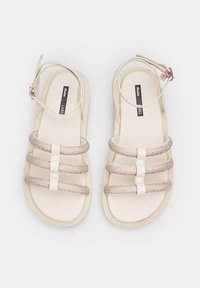 Beige sandaalid kolme metallist rihmaga ja pahkluu kinnitusega. Pehme tald ja minimalistlik disain, sobib igapäeva- või poolformaalseks kandmiseks.