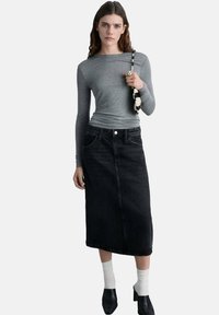 Grå langærmet bluse kombineret med en sort denimnederdel med høj talje. Outfittet har en simpel silhuet med en let stræk. Sorte sko og hvide sokker fuldender looket.